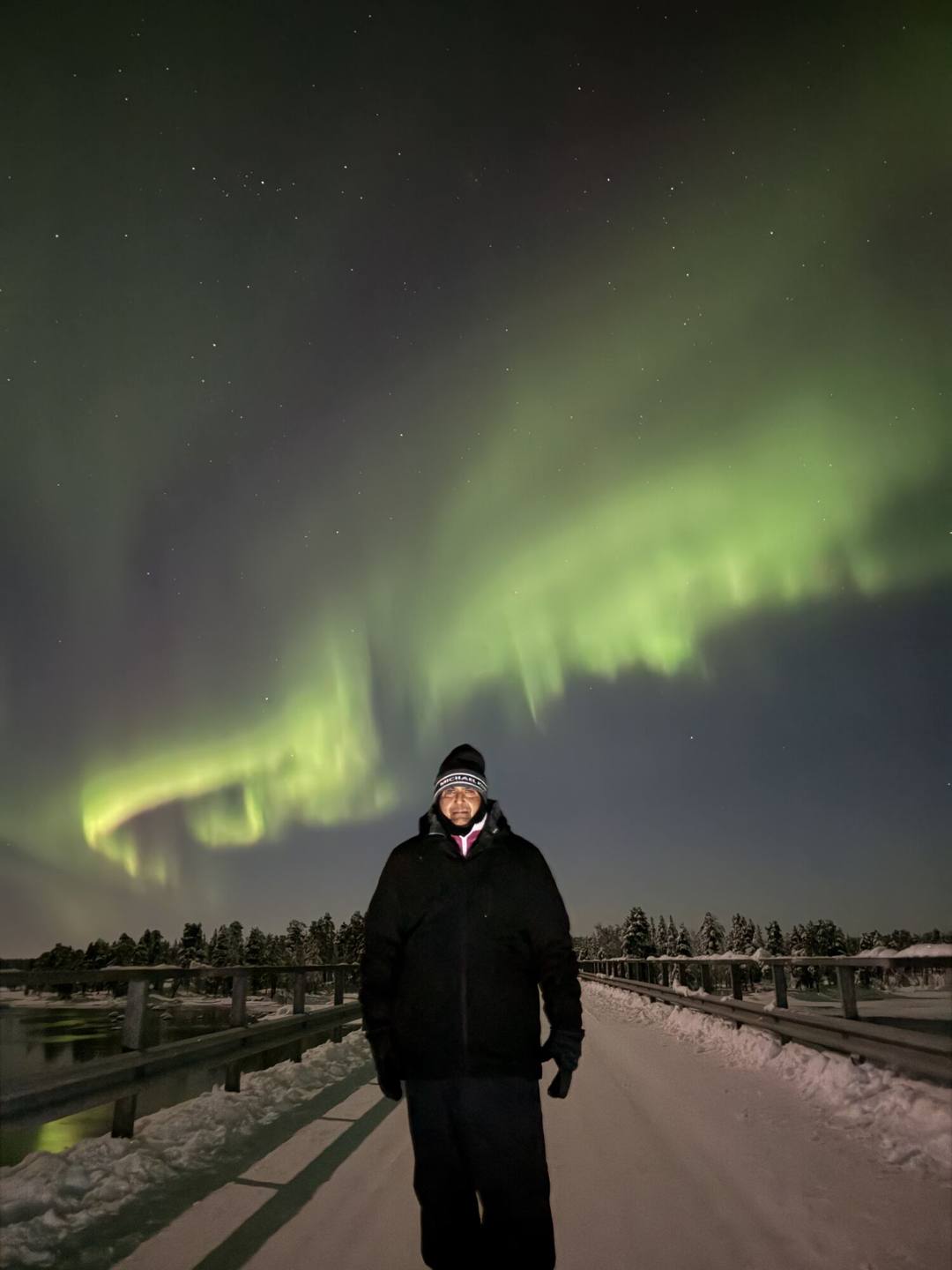 Guest standing on a snowy bridge under a green aurora